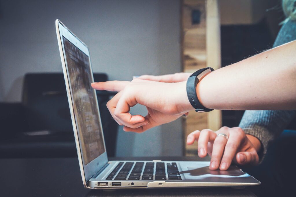 twee mensen achter de laptop waarbij 1 wijst naar het scherm. Horlogebandje om de pols